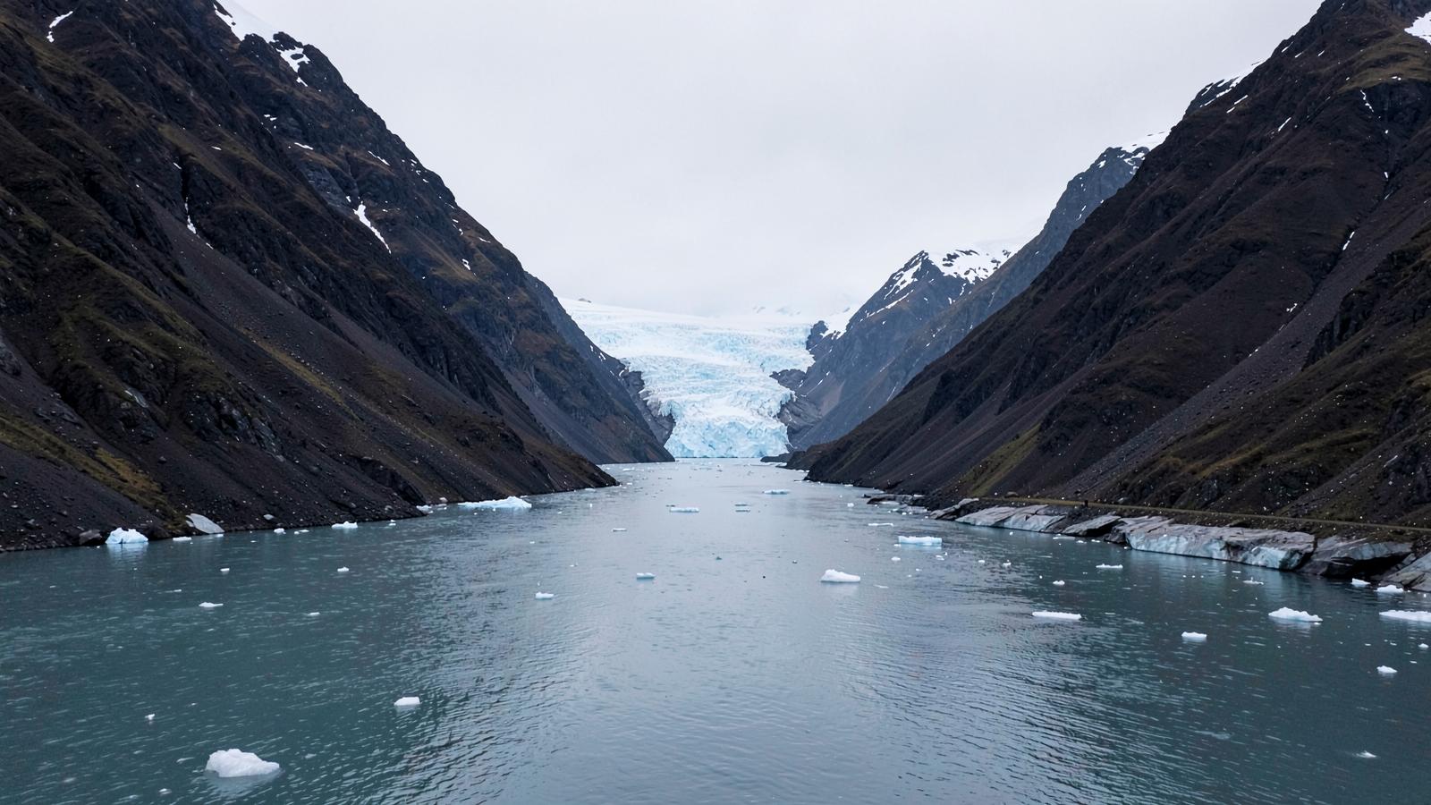 A narrow polar channel filled with brash ice between steep dark mountains and a glacier front
