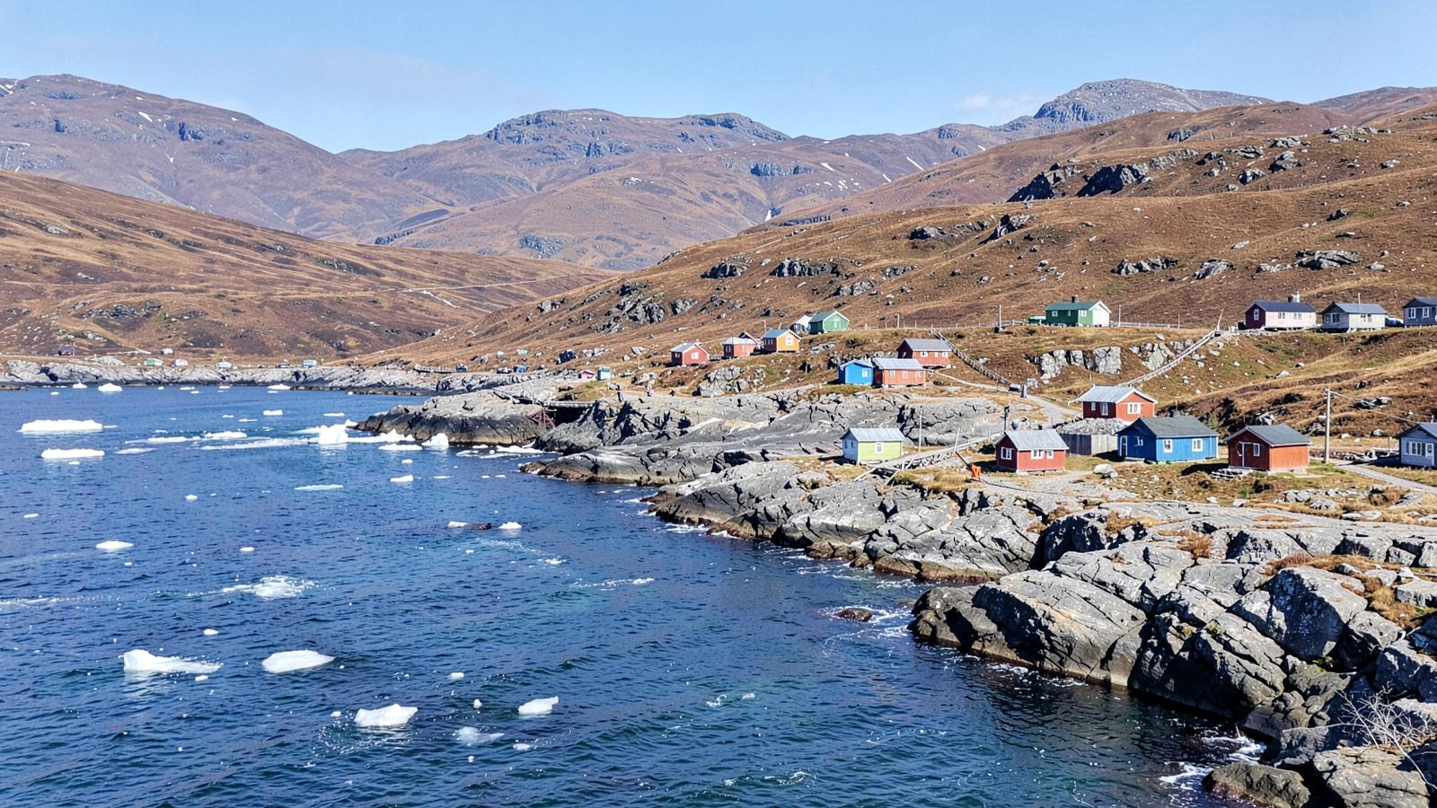 A small Arctic settlement of colourful wooden houses on bare rock beside a fjord with drifting ice