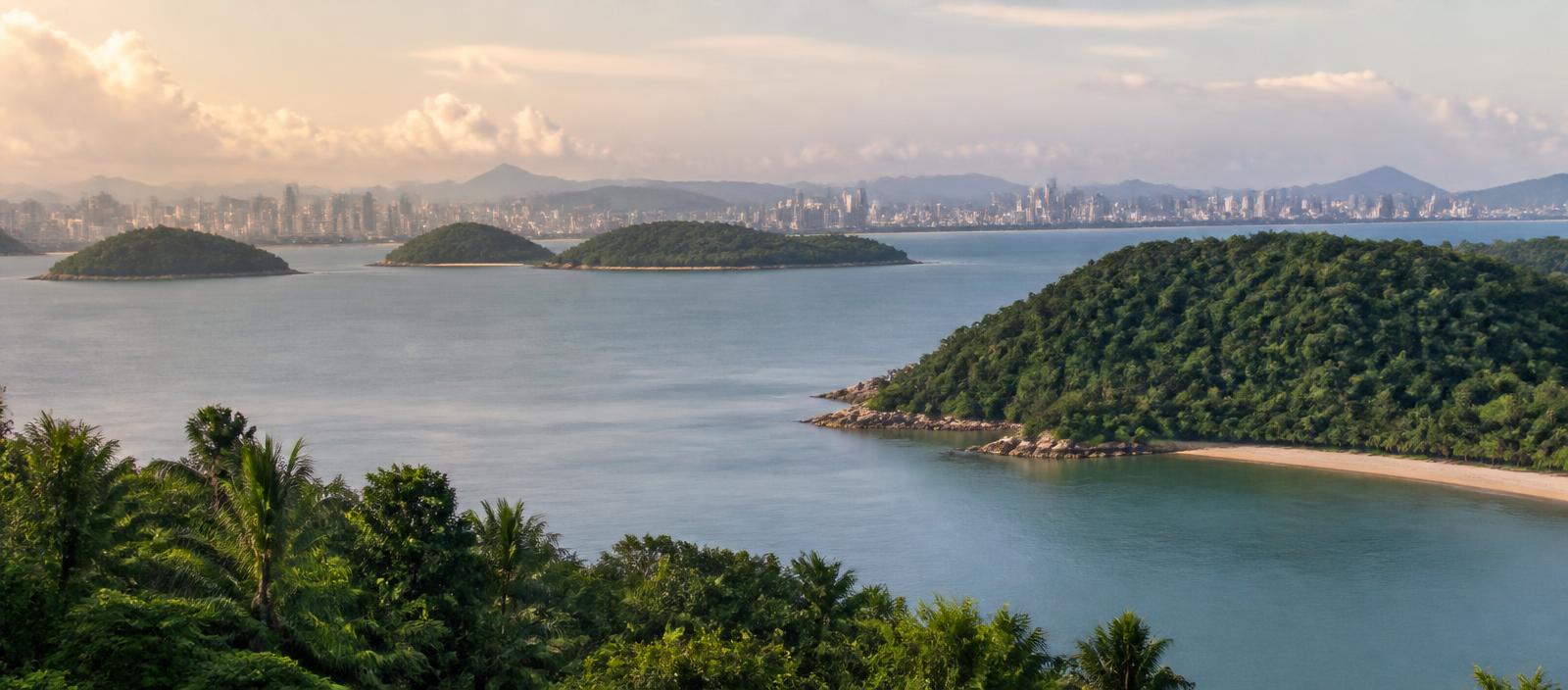 Forested tropical islands and a distant city skyline across calm coastal water in Southeast Asia