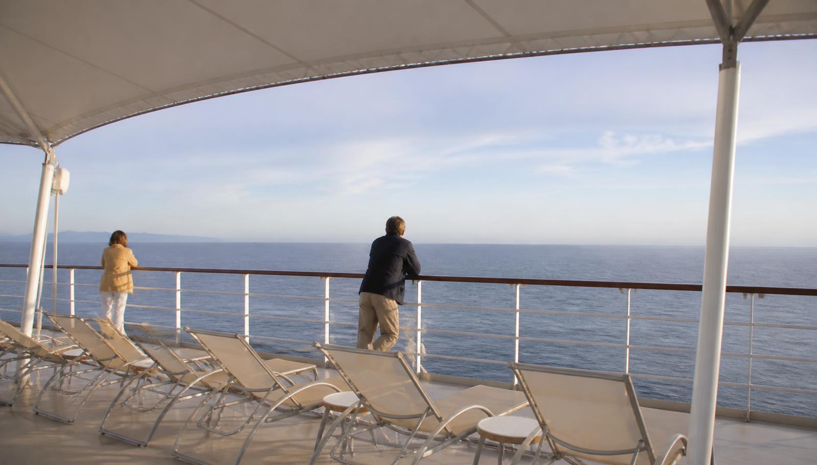 Passengers at the rail of an open deck looking out over calm open water