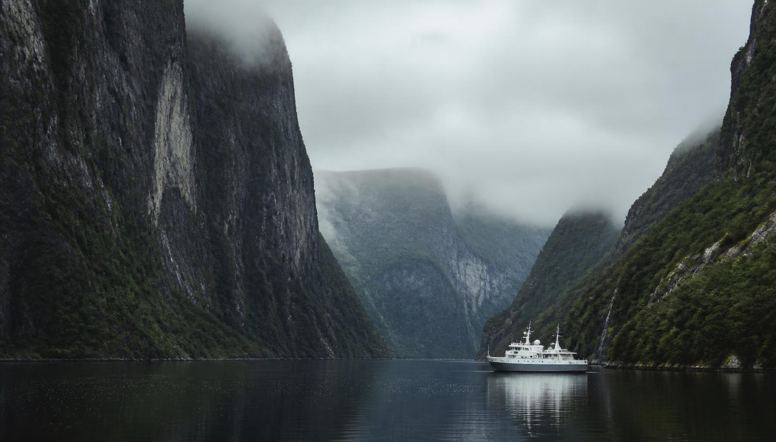 A small vessel in a narrow steep-sided waterway under low cloud