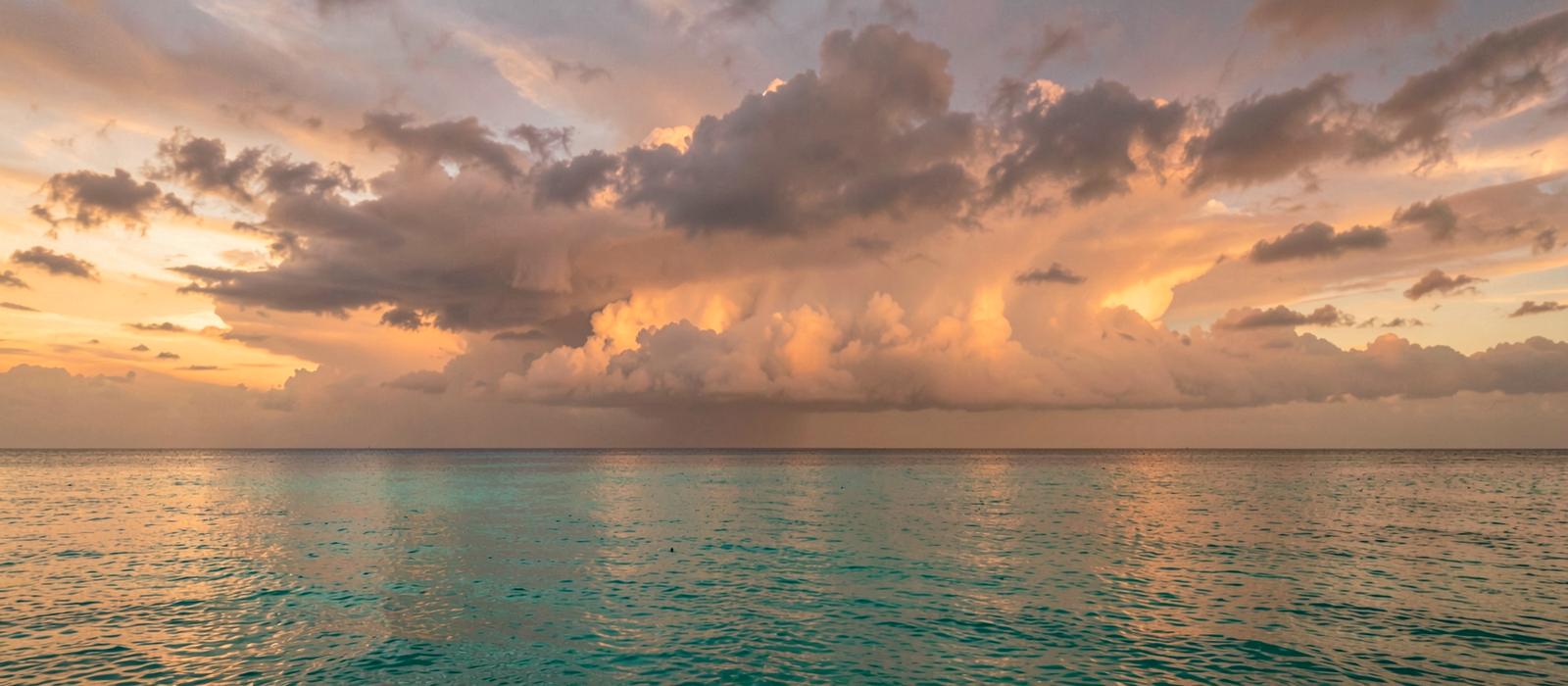 Tropical sea at dusk with a distant squall line on the horizon and calm turquoise water in the foreground